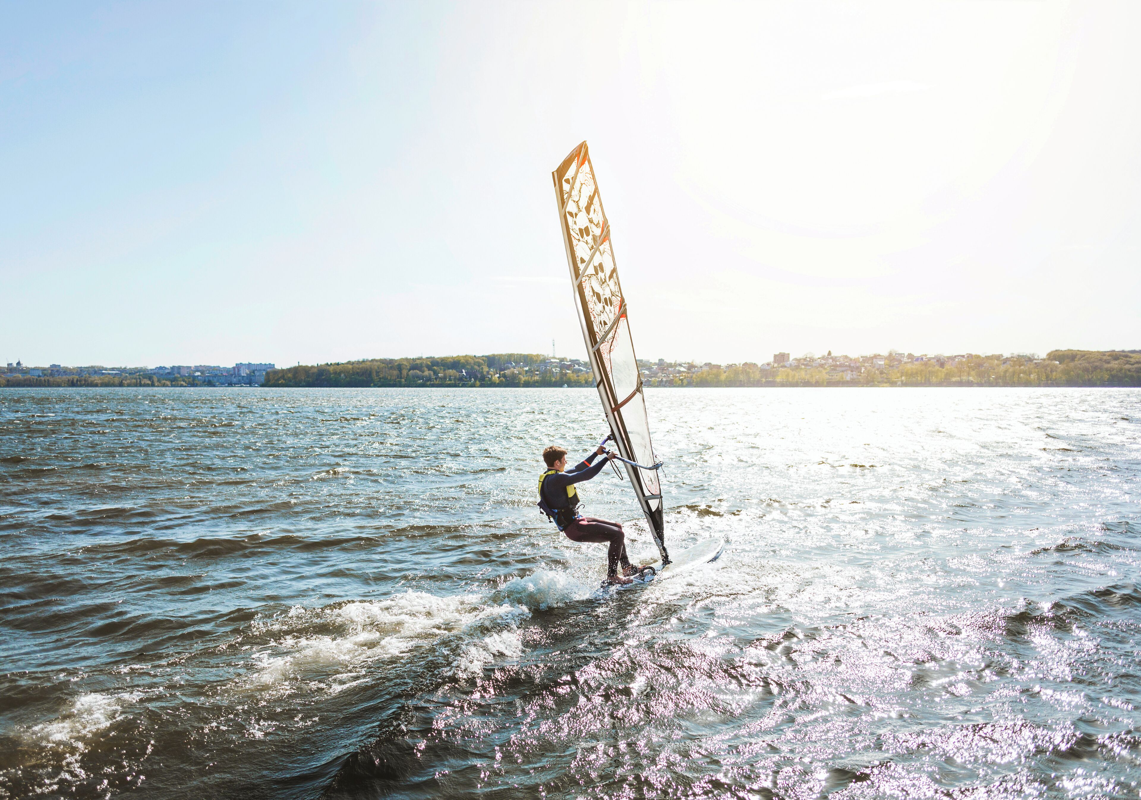 A person windsurfing on a body of water with a cityscape in the background.