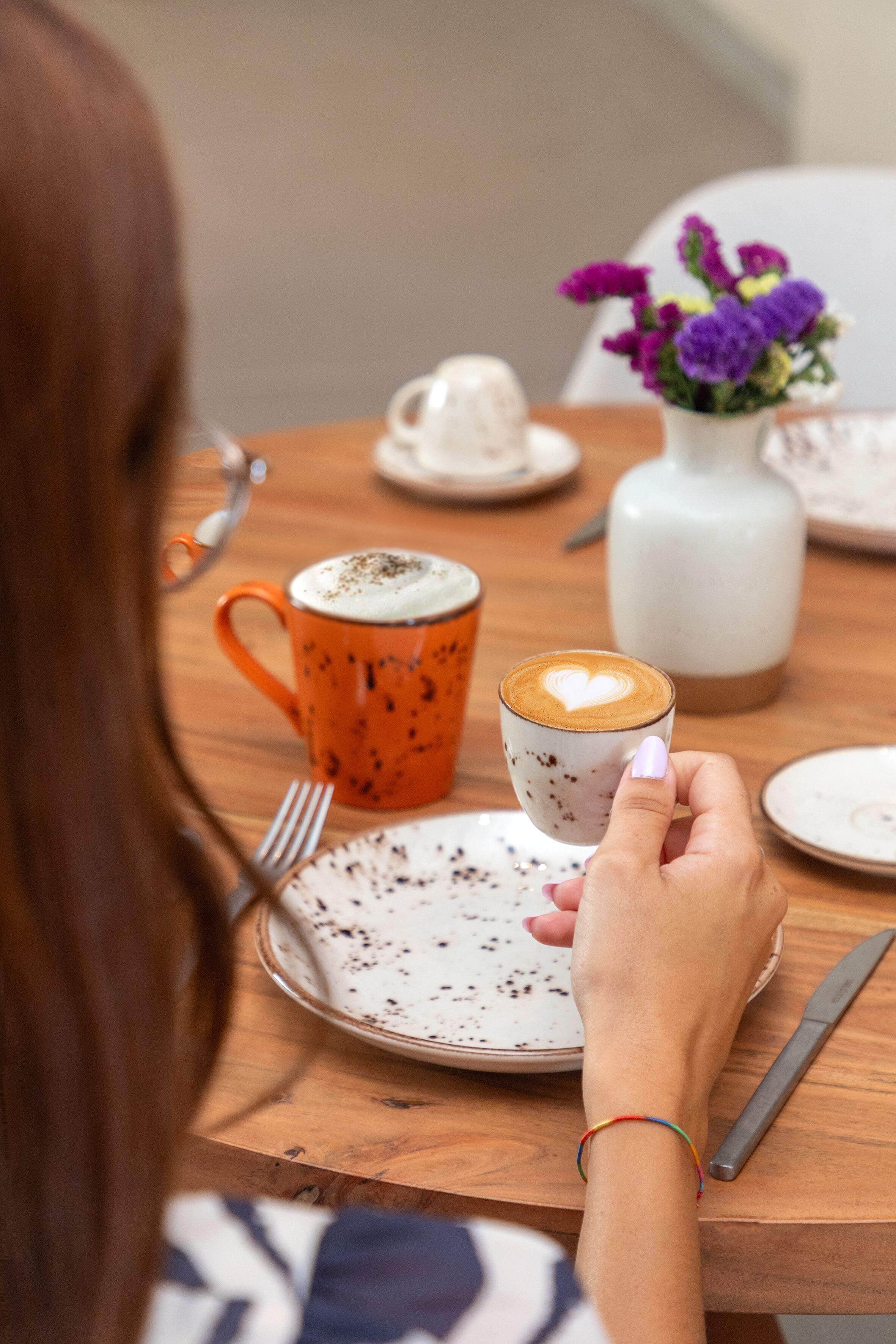 Una persona sentada a una mesa de madera con una taza de café y un plato de comida.