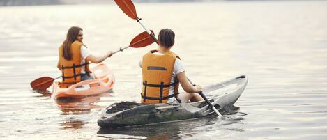 Two kayaks on calm water with people wearing life jackets.