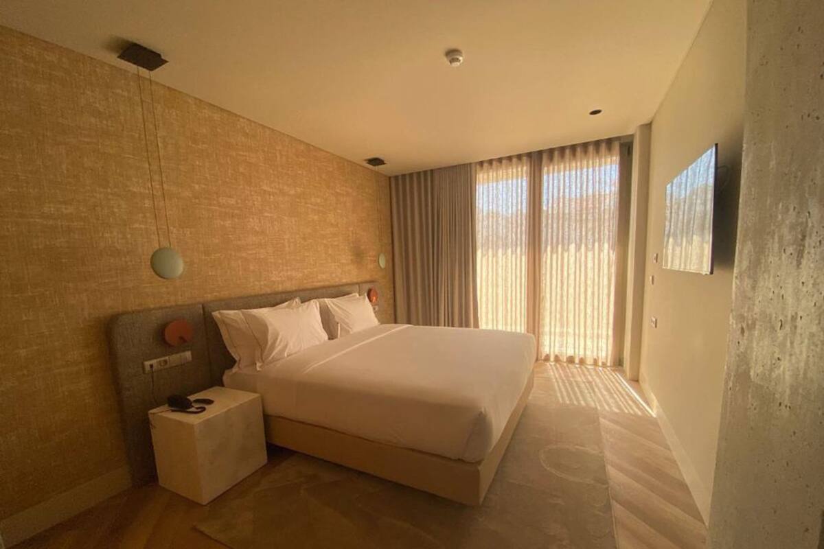 Een hotelkamer met een groot bed, een nachtkastje, een tv aan de muur en een raam met gordijnen.