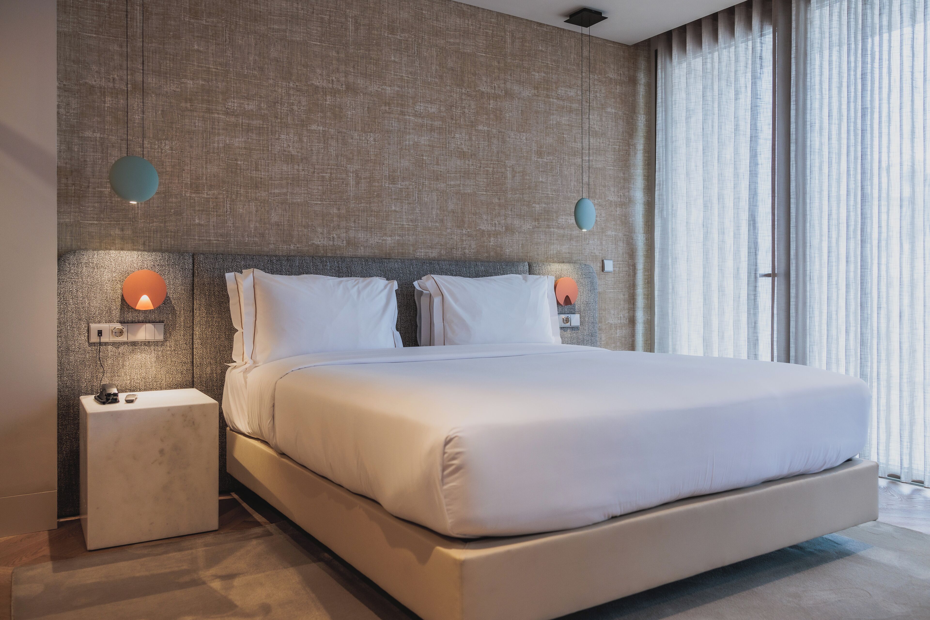 A modern bedroom with a large bed, two bedside tables, and a textured wall.