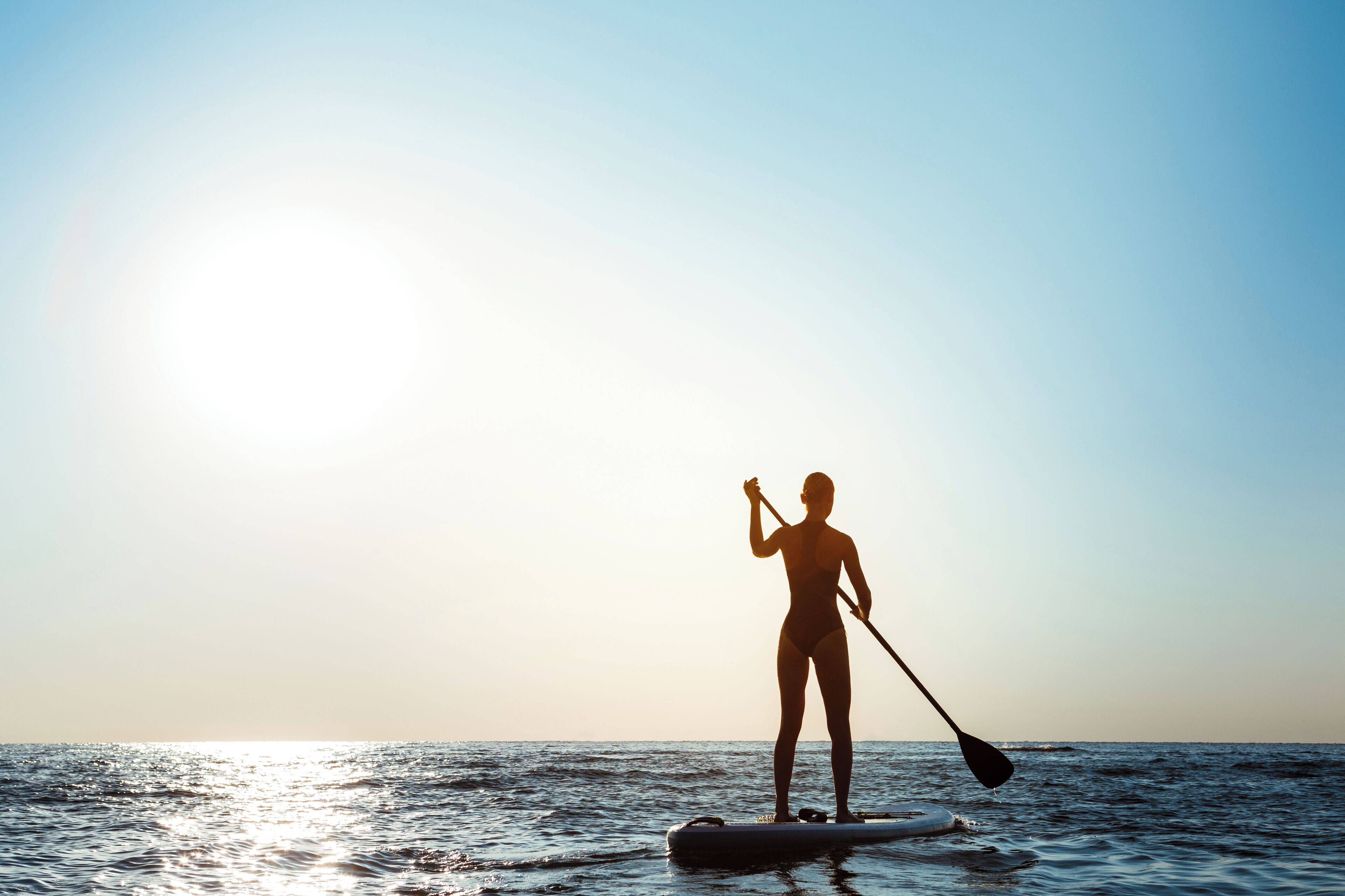 A person paddleboarding on calm waters during sunset.