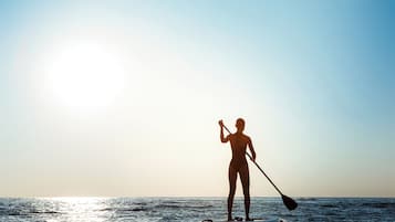 A person paddleboarding on calm waters during sunset.