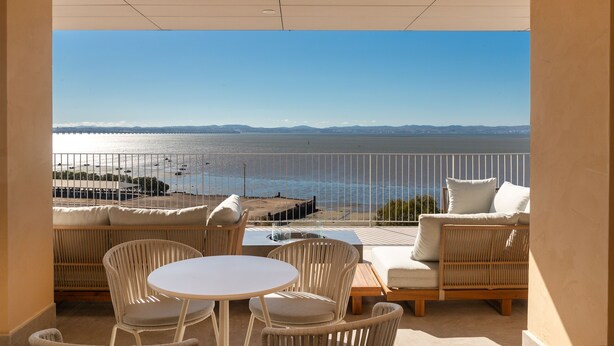 A balcony with wicker furniture, a round table, and a view of the sea and distant mountains. - Upon Vila Alcochete Hotel (Alcochete)