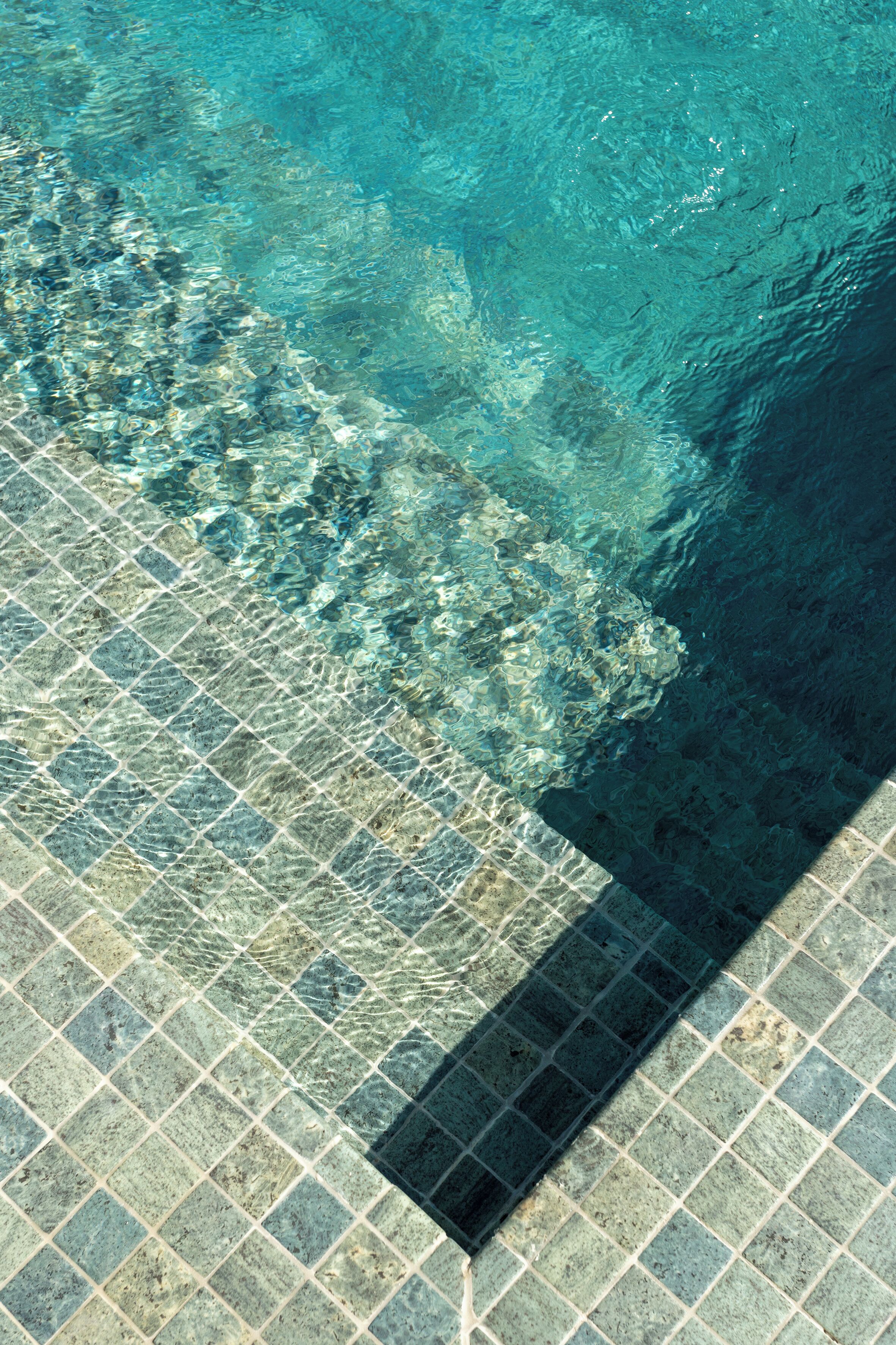 A clear view of a swimming pool with a tiled floor and a visible shadow cast by the pool's edge.