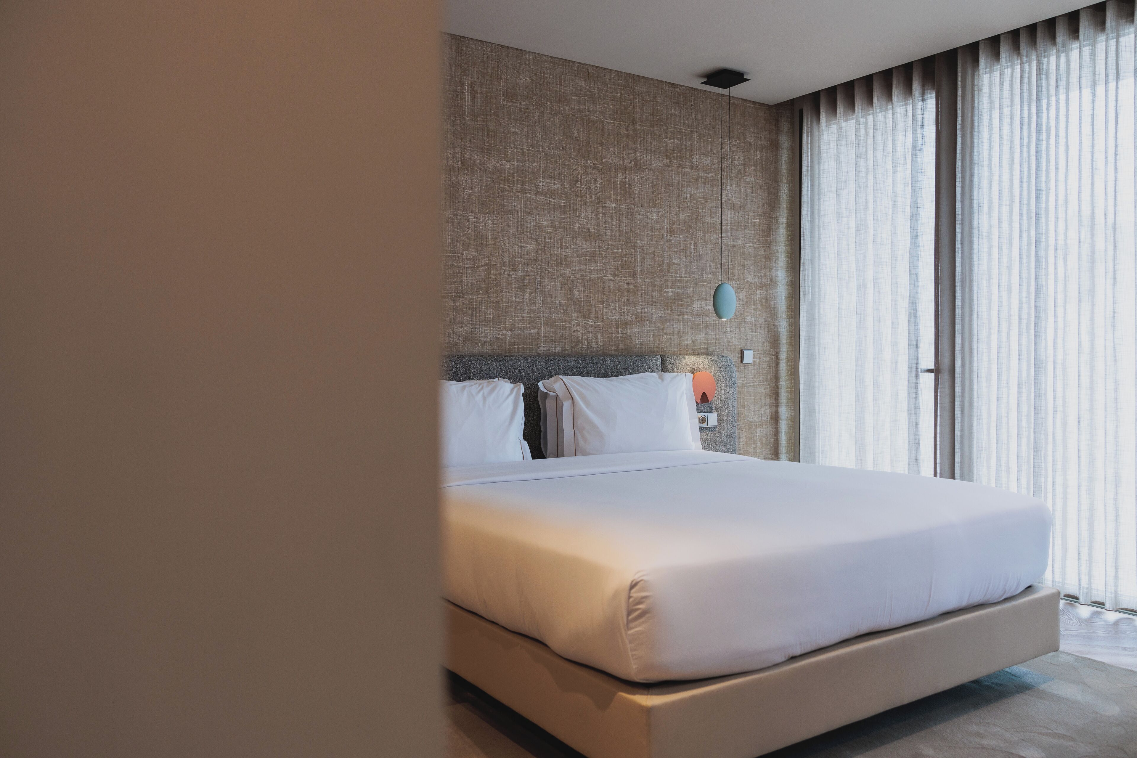 Une chambre d’hôtel moderne avec un grand lit, un mur à motifs et une grande fenêtre avec des rideaux.