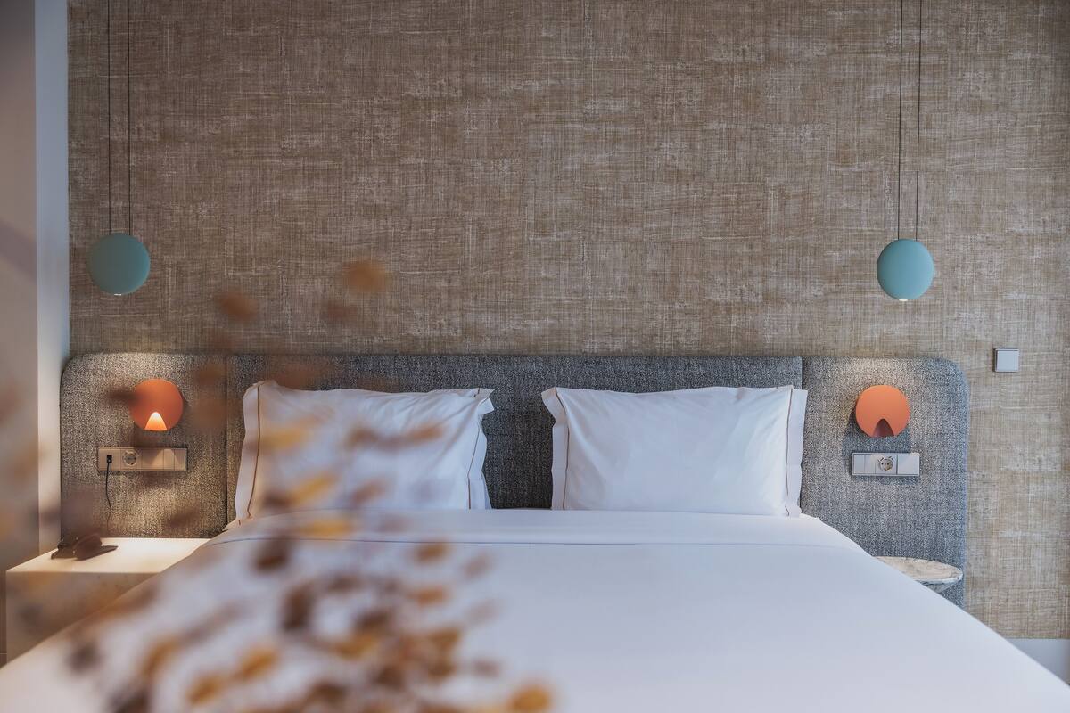 Een net opgemaakt bed met witte lakens, twee kussens en een hoofdbord met een structuur.
