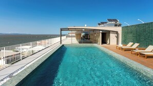 A rooftop infinity pool with a glass enclosure, lounge chairs, and solar panels. - Upon Vila Alcochete Hotel (Alcochete)