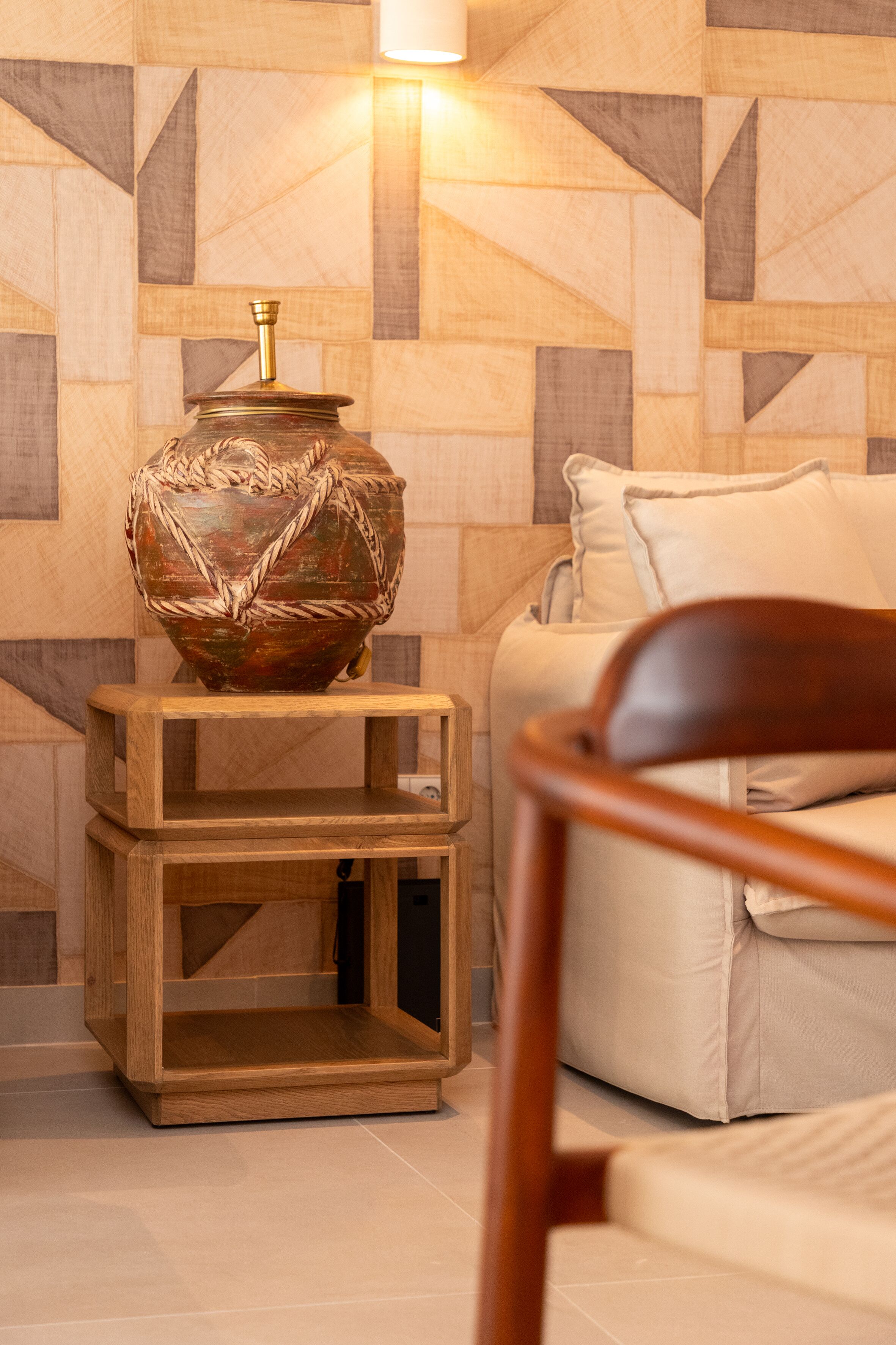 A modern living room with a geometric-patterned wall, a wooden side table with a decorative vase, and a beige sofa.