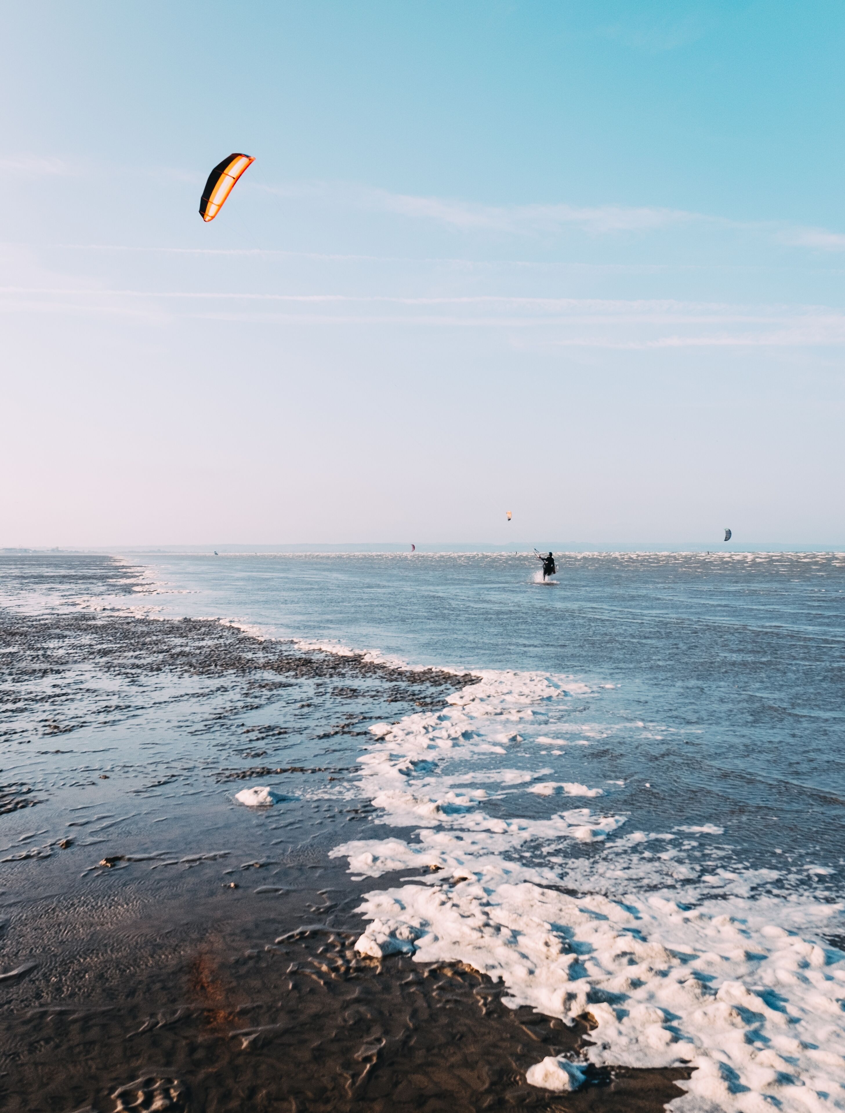 A beach with a person kite surfing, a distant shoreline, and a clear sky.