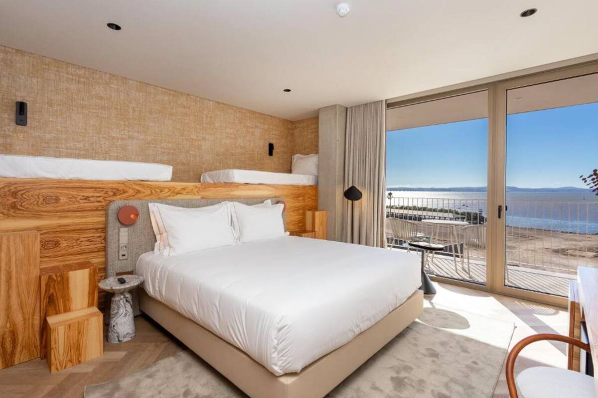 Een moderne hotelkamer met een groot bed, houten hoofdeinde en een balkon met uitzicht op het strand en de zee.