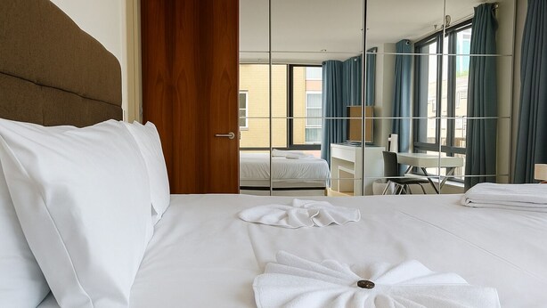 A hotel room with a large bed, a wooden door, a desk, and a chair. - Still Life Warren Street (London)