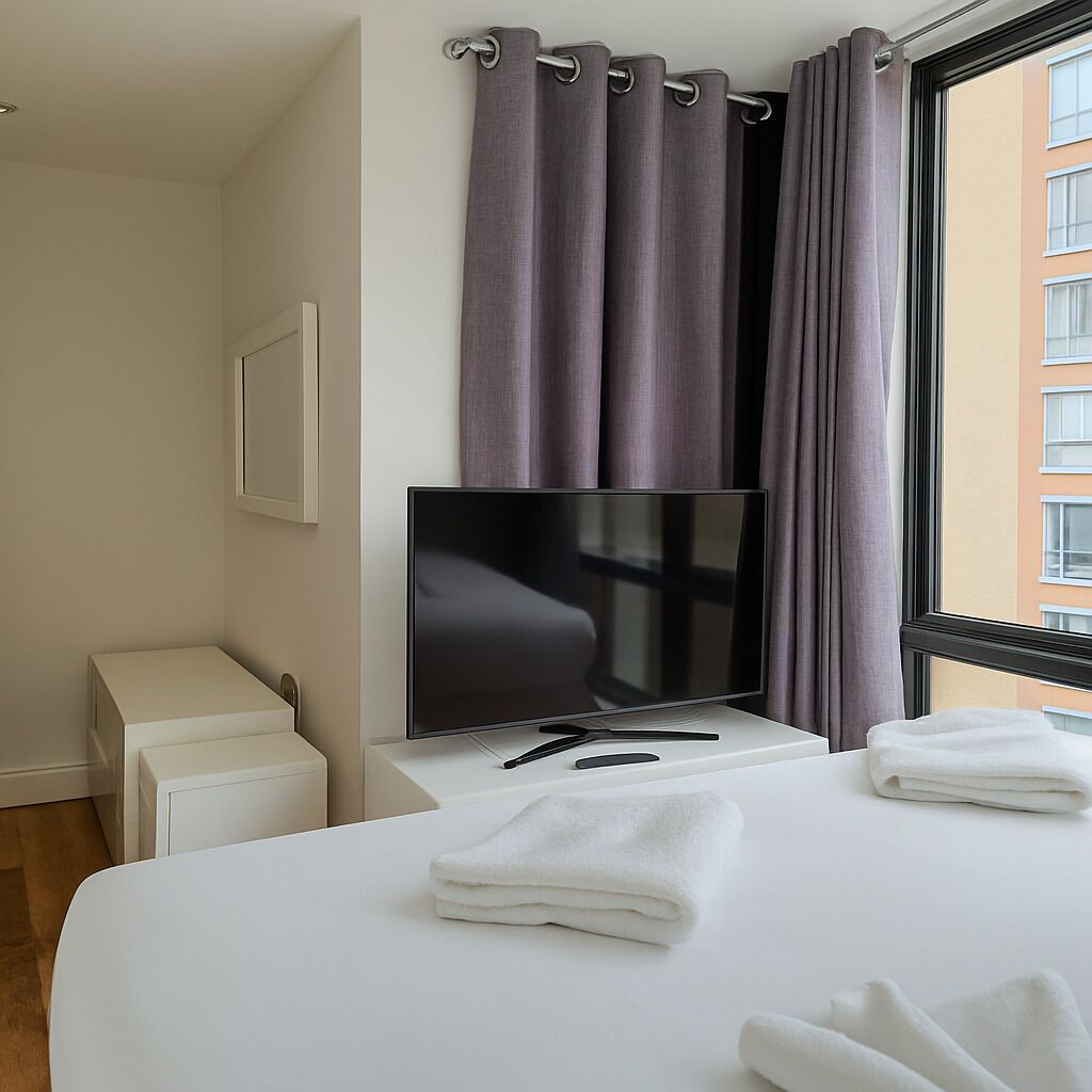 Une chambre d’hôtel avec un lit, une télévision, une petite table et une fenêtre avec des rideaux.