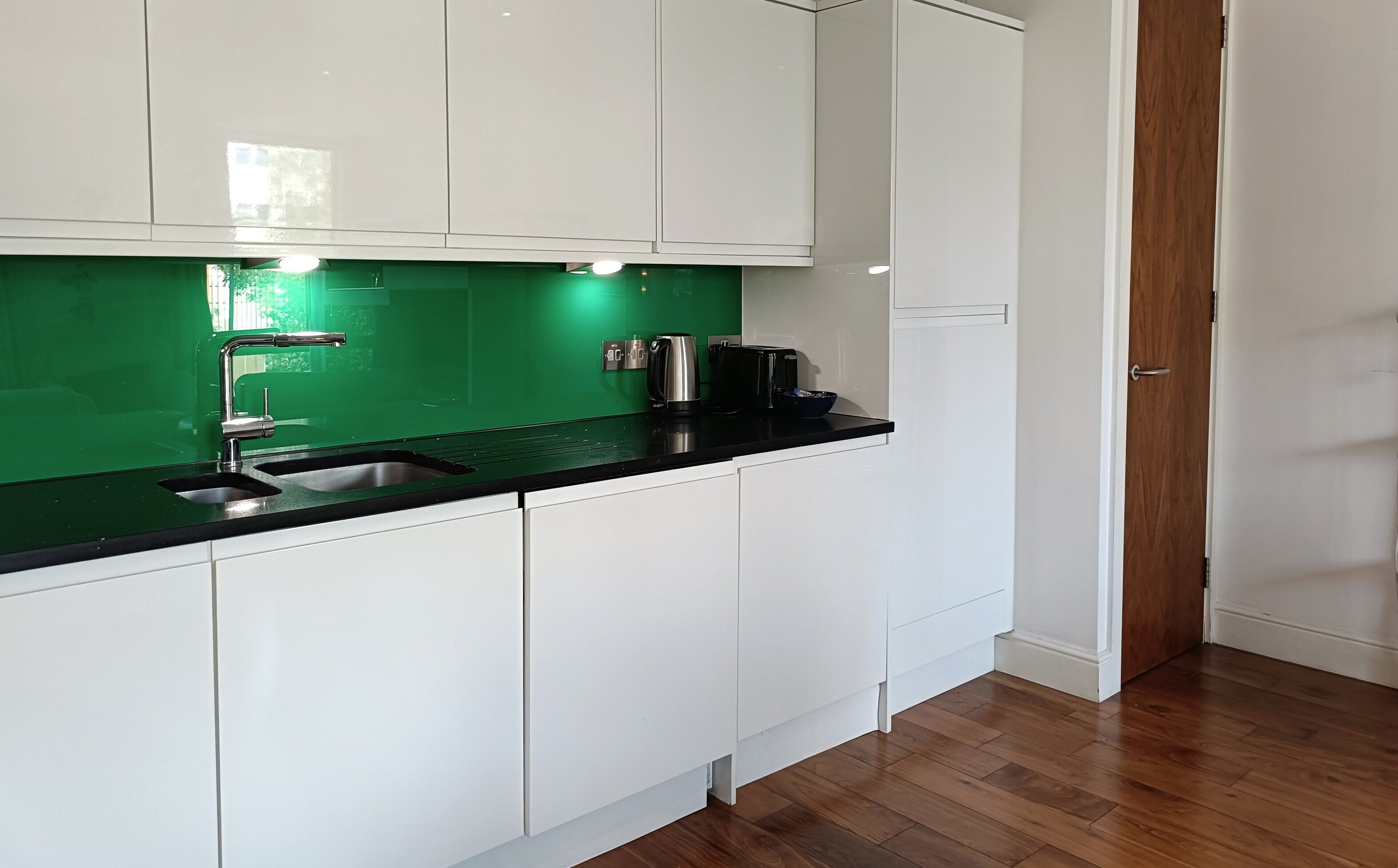 A modern kitchen with white cabinets, a black countertop, and a green backsplash.