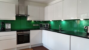 A modern kitchen with white cabinets, a black countertop, a stainless steel range hood, a microwave, and a built-in oven. - Still Life Warren Street (London)