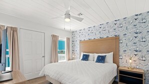 Ein Schlafzimmer mit Bett, Deckenventilator, Nachttisch und einer Wand mit maritimem Wandpapier.
