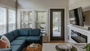 Una sala moderna con un sofá modular, una mesa de comedor con posavasos, un reposapiés de mimbre y una chimenea.