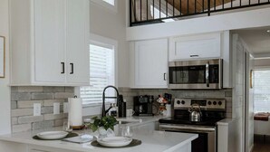 Una cocina moderna con armarios blancos, una isla central, taburetes de madera y una estufa de acero inoxidable.