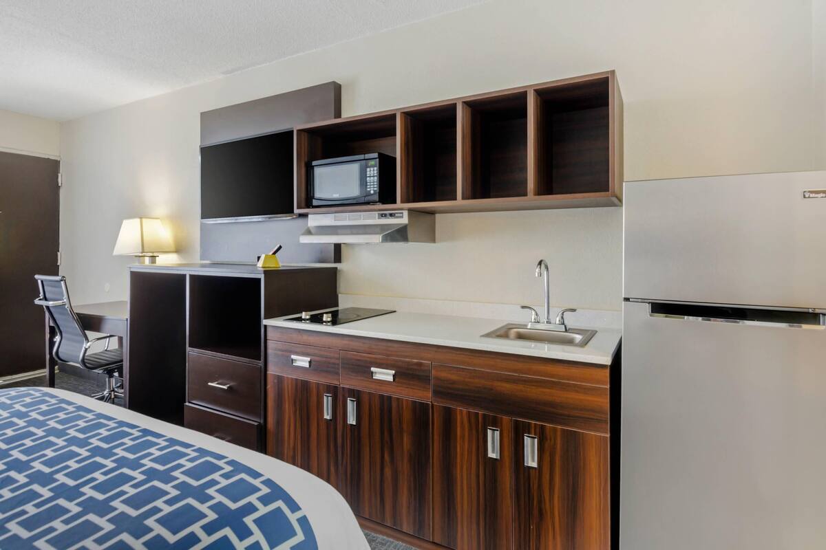A hotel room with a bed, a desk, a microwave, a refrigerator, and a sink.