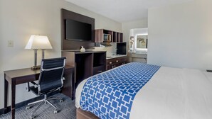 Habitación de hotel con cama, escritorio con silla, televisión, microondas y un baño pequeño.