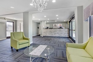 Un hall de hotel con mostrador de recepción, dos sillones, una mesa de centro de vidrio y una araña.