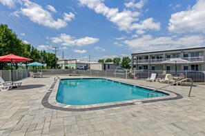 A swimming pool with lounge chairs and umbrellas, surrounded by a fenced area and a building with balconies. - Suburban Studios Verona - Staunton North (Verona)