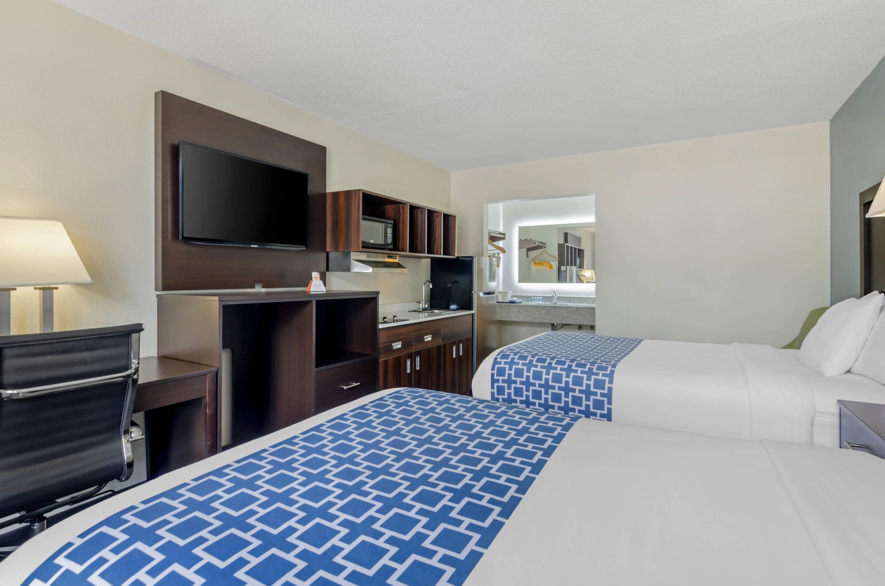 A hotel room with two beds, a TV, a microwave, a sink, and a mirror.