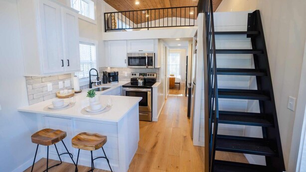 A modern kitchen with white cabinetry, a central island with stools, a black staircase, and a loft area with a railing.