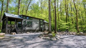 A cabin with a porch, a gravel driveway, and a forested backdrop. - Sage Cabin by Creekside Hideaway (Gatlinburg)