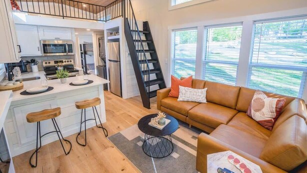 A modern kitchen with a central island, a staircase, and a living area with a sofa and coffee table. - Sage Cabin by Creekside Hideaway (Gatlinburg)
