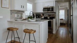 A modern kitchen with white cabinetry, a central island with stools, a microwave, oven, and a sink. - Sage Cabin by Creekside Hideaway (Gatlinburg)