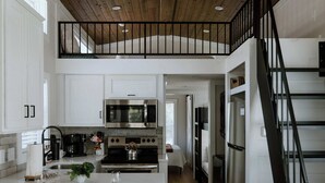 A modern kitchen with white cabinetry, a wooden ceiling, and a central island with stools. - Willow Cabin by Creekside Hideaway (Gatlinburg)
