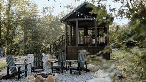 A wooden cabin with a deck and outdoor seating area, surrounded by trees and rocks.