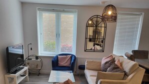 A modern living room with a blue armchair, a beige sofa, a coffee table, and a TV on a stand. - Captivating 2-bed Apartment in Glasgow (Glasgow)