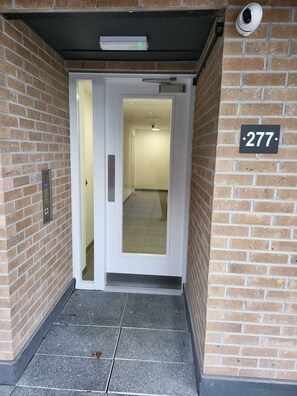 A building entrance with a brick wall, a door with a glass panel, and a number sign '277'. - Captivating 2-bed Apartment in Glasgow (Glasgow)