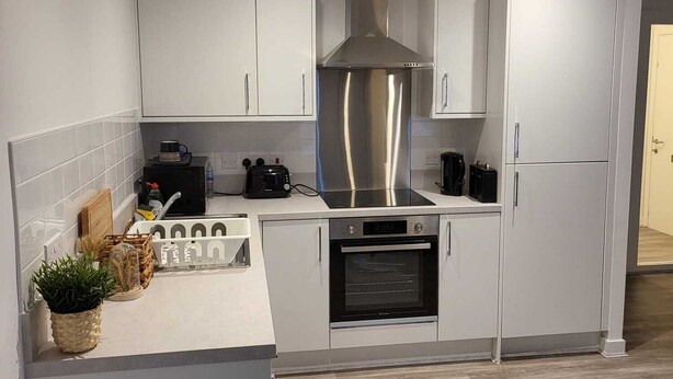 A modern kitchen with white cabinets, a stainless steel range hood, an oven, and a built-in microwave. - Captivating 2-bed Apartment in Glasgow (Glasgow)