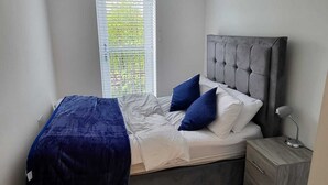 A bedroom with a bed, a nightstand, a window with blinds, and a ceiling light. - Captivating 2-bed Apartment in Glasgow (Glasgow)