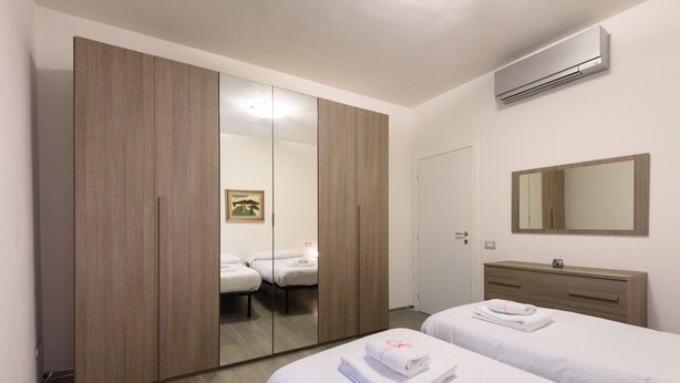A hotel room with a large wardrobe, a bed with neatly folded towels, a bedside table, a mirror, and an air conditioning unit. - Guelfa 14 - Two Bedroom Apartment, Sleeps 4 (Firenze)