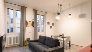 A modern living room with a grey sofa, a dining table with chairs, a small side table, and a radiator. - Guelfa 14 - Two Bedroom Apartment, Sleeps 4 (Firenze)