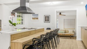 Cozinha moderna com ilha central, área de refeições com cadeiras, um sofá e um ventilador de teto.