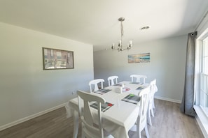 Uma sala de jantar com mesa e cadeiras brancas, um candelabro e obras de arte nas paredes.