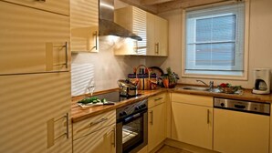 A kitchen with wooden cabinets, a built-in oven, a sink, and a window with blinds. - FH Falster XXL im Schlosspark Bad Saarow, 178m², 8+4 Pers, Sauna,Whirlpool,Kamin (Bad Saarow)