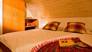 A bedroom with a wooden ceiling, a bed with a red and gold patterned bedspread, two plaid pillows, and a shelf with a red bag. - FH Falster XXL im Schlosspark Bad Saarow, 178m², 8+4 Pers, Sauna,Whirlpool,Kamin (Bad Saarow)