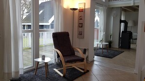 A room with a large sliding glass door leading to a balcony, a dark blue rug, a wooden chair, a small round table, and a floor lamp. - FH Falster XXL im Schlosspark Bad Saarow, 178m², 8+4 Pers, Sauna,Whirlpool,Kamin (Bad Saarow)