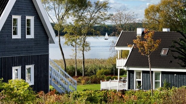 Ein Haus mit einem steilen Dach, einer sichtbaren Treppe und Blick auf einen See mit einem Segelboot.