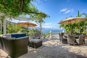 An outdoor patio with wicker furniture, umbrellas, and a view of the ocean. - VILLA W/POOL,CHEF, PANORAMIC OCEANVIEWS, 7 BR (Puerto Vallarta)