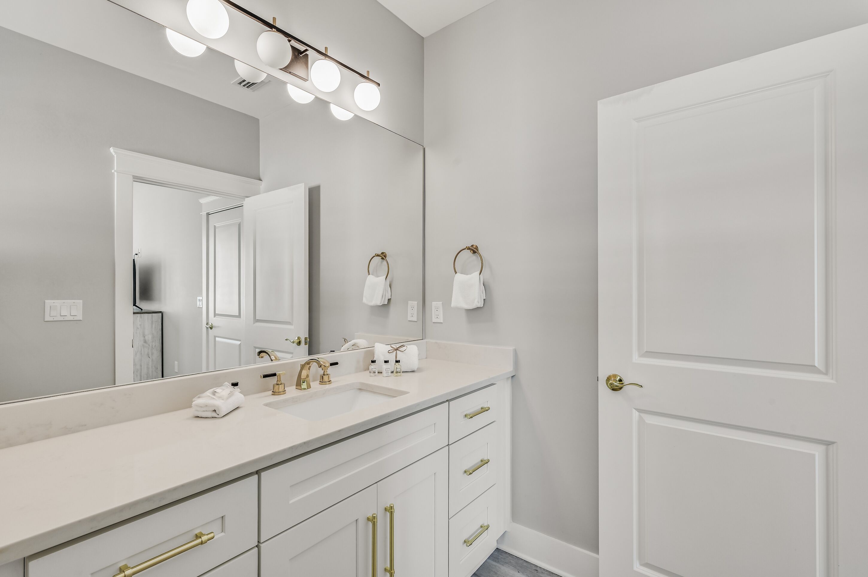 A modern bathroom with a large mirror, a white sink, gold fixtures, and a door with a brass handle.