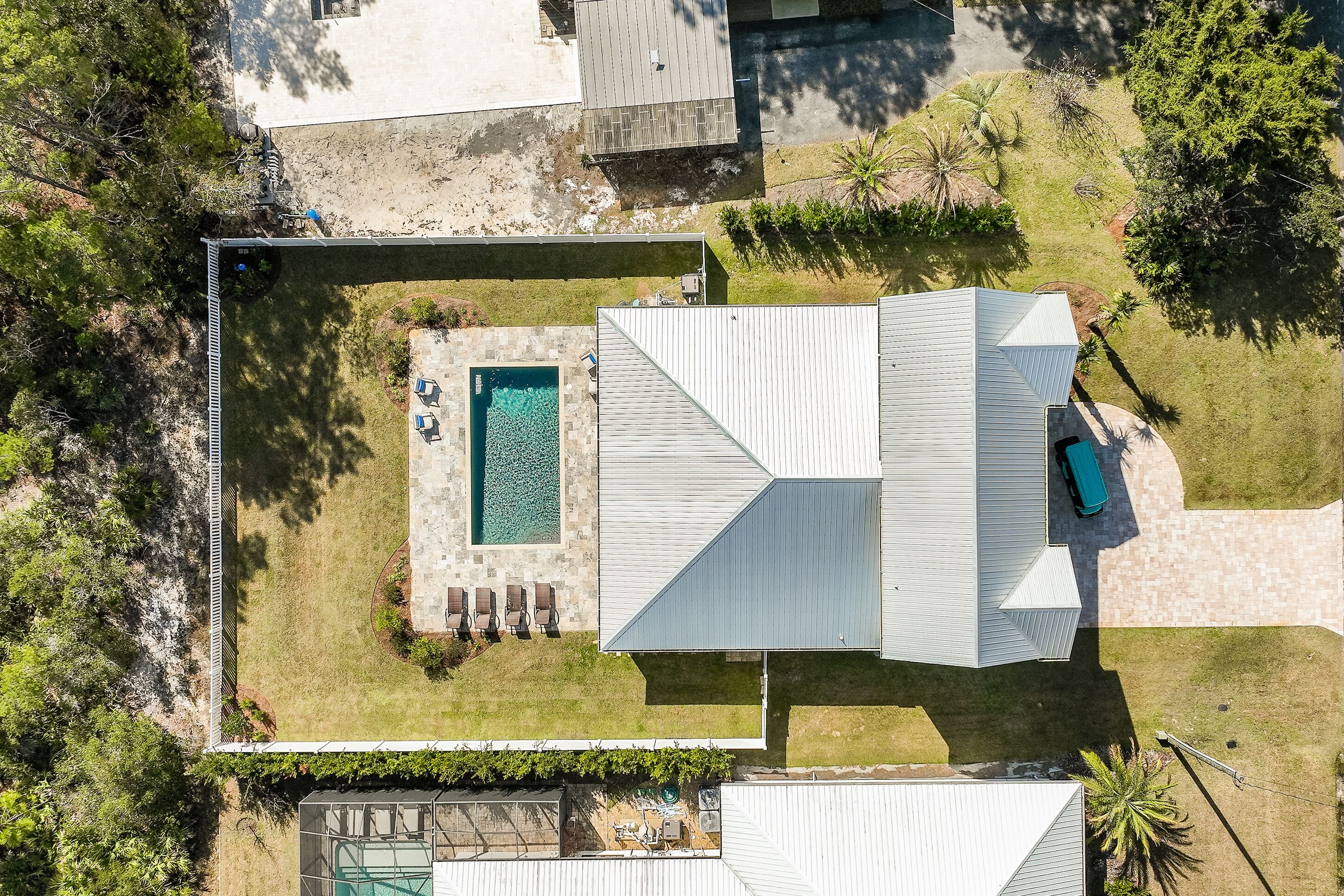 An aerial view of a modern house with a swimming pool, a covered patio, and a well-maintained lawn.