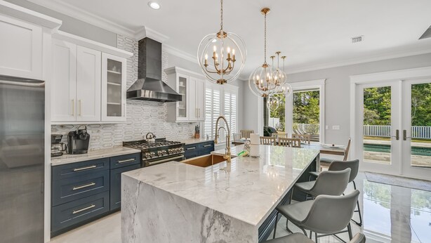 A modern kitchen with white cabinets, a large island, stainless steel appliances, and a view of the outdoors.