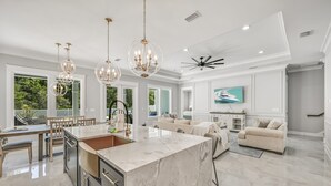 A spacious kitchen with a marble island, pendant lighting, and a dining area with a view of the outdoors.